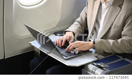 Cropped shot of professional businessman working with laptop in airplane during flight 117473045