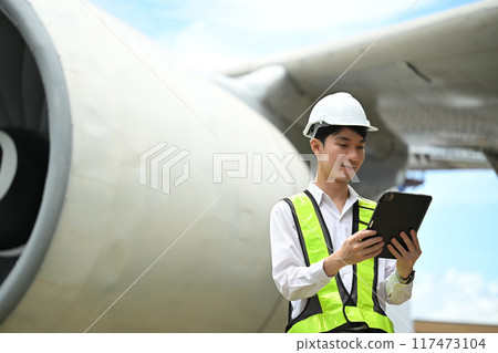 Young male engineer or aviation technician using digital tablet in front of large aircraft engine Young male engineer or aviation technician using digital tablet in front of large aircraft engine 117473104