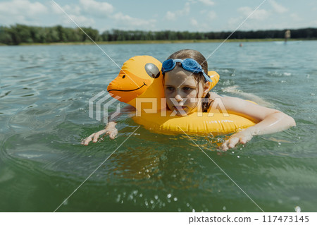 Carefree summer day: a girl with an inflatable duck float in the lake. She is enjoying the refreshing water and the sunny weather 117473145