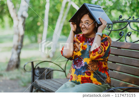 Joyful woman using her laptop as a makeshift umbrella in the park Tech-friendly environment as woman finds an unconventional use for her computer. Joyful woman using her laptop as a makeshift umbrella in the park Tech-friendly environment as woman finds an unconventional use for her computer. 117473155