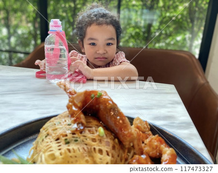 Cute little girl drinking water from plastic bottle while eating Thai style fried shrimp with bean sprouts and sweet and sour sauce with water bottle in restaurant 117473327