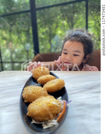 Cute Asian little girl eating deep fried shrimp nuggets in cafe 117473481