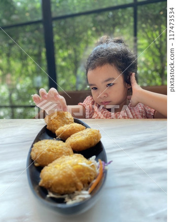 Little Asian girl eating deep fried shrimp nuggets on the table at home Little Asian girl eating deep fried shrimp nuggets on the table at home 117473534