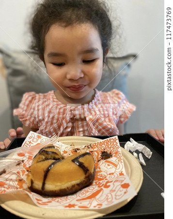 Cute little girl eating a donut with a spoon Cute little girl eating a donut with a spoon 117473769