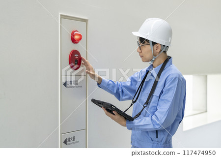 A man in work clothes checking the fire alarm, building maintenance image 117474950
