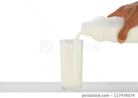 Hand holding bottle of milk pouring into glass on white table on white background 117476074