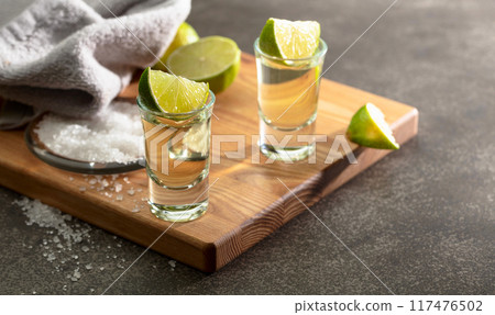 Tequila with sea salt and lime slices on a cutting board. 117476502