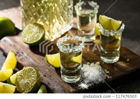 Tequila with sea salt and lime slices on a old cutting board. 117476503