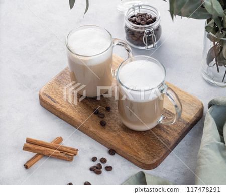 Two cappuccino or latte with milk foam in glasses on a light background with coffee beans 117478291