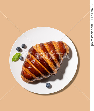 Freshly baked croissant  on a white plate and blueberries on a yellow background. 117478292