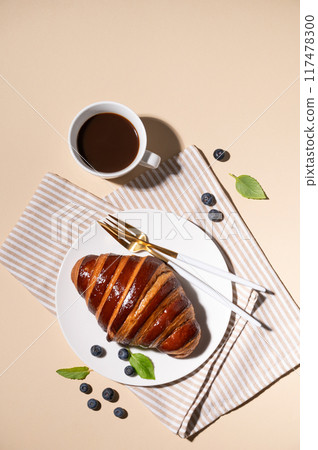 Freshly baked croissant with chocolate on a white plate and blueberries on a yellow background Freshly baked croissant with chocolate on a white plate and blueberries on a yellow background 117478300