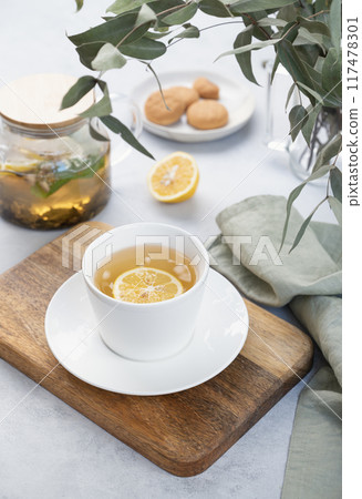 Herbal tea with lemon and mint in a white cup on a wooden plate on a light background  117478301