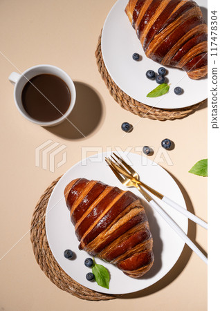 Freshly baked croissants with chocolate on a white plate and blueberries on a yellow background  117478304