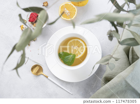 Herbal tea with lemon and mint in a white cup on a light background with eucalyptus branches. Herbal tea with lemon and mint in a white cup on a light background with eucalyptus branches. 117478305
