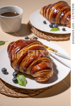 Freshly baked croissants with chocolate on a white plate and blueberries on a yellow background Freshly baked croissants with chocolate on a white plate and blueberries on a yellow background 117478306