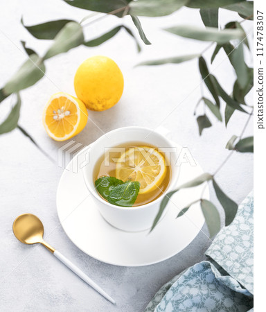 Herbal tea with lemon and mint in a white cup on a light background with eucalyptus branches.  117478307