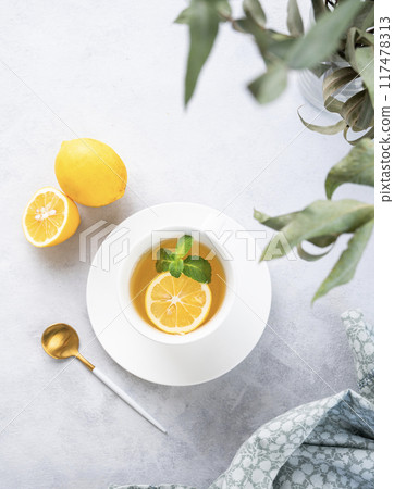 Herbal tea with lemon and mint in a white cup on a light background with eucalyptus branches  117478313