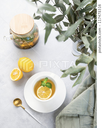 Herbal tea with lemon and mint in a white cup on a wooden plate on a light background  117478316