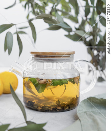 Glass teapot of herbal tea with lemon, ginger and mint on a light background  117478320