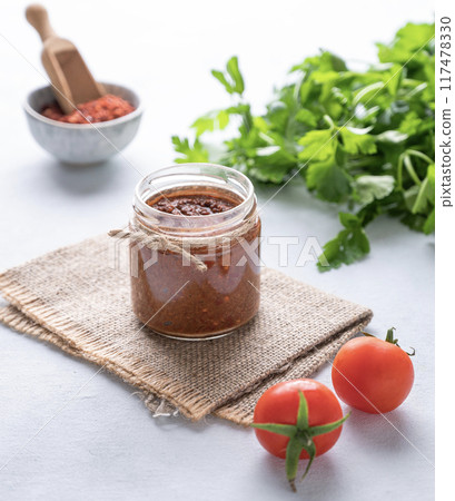 Hot sauce adjika. Homemade appetizer with pepper and tomatoes in a jar on light background  117478330