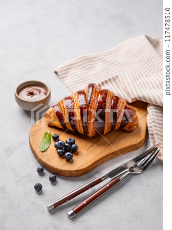 Fresh croissant with chocolate on a cutting board on a light background with a blueberries. Fresh croissant with chocolate on a cutting board on a light background with a blueberries. 117478510