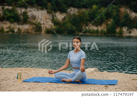 Engaging in a Serene Yoga Practice by the Tranquil Water Surrounded by Natures Beauty Engaging in a Serene Yoga Practice by the Tranquil Water Surrounded by Natures Beauty 117479197