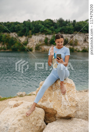A Young Girl Delightfully Enjoying the Beauty of Nature While Holding a Drink and Using Her Phone 117479200
