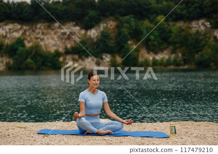 A Woman Engaged in Meditative Practice by a Serene and Tranquil Lake Surrounded by Nature 117479210