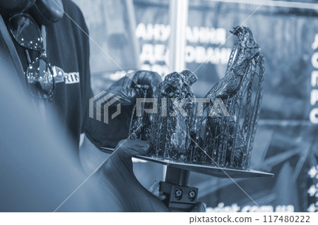 Black model with supports printed on 3D printer close-up. Man holding in hand object created on 3D printer from hardened rubber under influence of ultraviolet light. SLA 3D printing. Stereolithography 117480222
