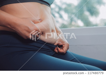 fat woman, fat belly, chubby, obese woman hand holding excessive belly fat with measure tape, woman diet lifestyle concept 117480779
