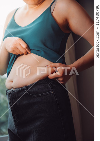 fat woman, fat belly, chubby, obese woman hand holding excessive belly fat with measure tape, woman diet lifestyle concept fat woman, fat belly, chubby, obese woman hand holding excessive belly fat with measure tape, woman diet lifestyle concept 117480796