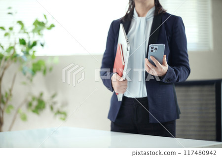 Middle-aged woman standing with a smartphone in the office 117480942