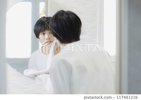 Young man looking in the mirror in the bathroom Young man looking in the mirror in the bathroom 117481216