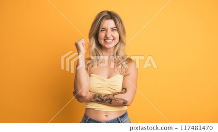 Smiling and jumping young woman with raised hands on yellow background Smiling and jumping young woman with raised hands on yellow background 117481470