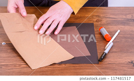 Step by step. Teacher guides online class through making a paper puppet from a brown bag, creatively using a wooden surface as a workspace. Step by step. Teacher guides online class through making a paper puppet from a brown bag, creatively using a wooden surface as a workspace. 117481517