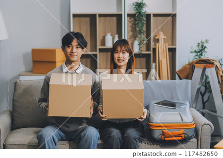 Young Asian couple relocating to a new house, joyfully packing and unpacking belongings. Expertise in moving, packing, togetherness, and creating a new home together. Young Asian couple relocating to a new house, joyfully packing and unpacking belongings. Expertise in moving, packing, togetherness, and creating a new home together. 117482650