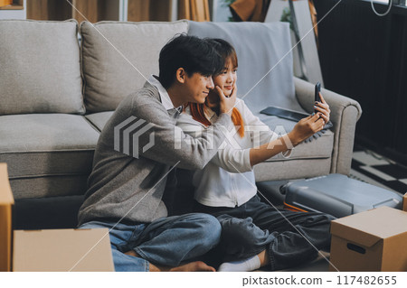 Young Asian couple relocating to a new house, joyfully packing and unpacking belongings. Expertise in moving, packing, togetherness, and creating a new home together. 117482655