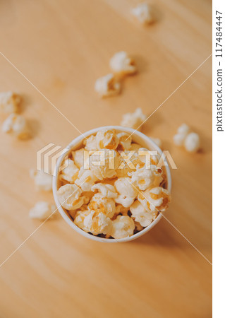 A bucket of popcorn, top-view, warm colors, light brown wooden background, flat lay, daylight macro close-up 117484447