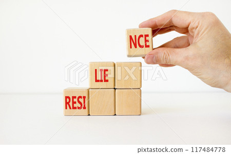 Resilience symbol. Concept word Resilience on beautiful wooden cubes. Businessman hand. Beautiful white background. Business resilience concept. Copy space. Resilience symbol. Concept word Resilience on beautiful wooden cubes. Businessman hand. Beautiful white background. Business resilience concept. Copy space. 117484778