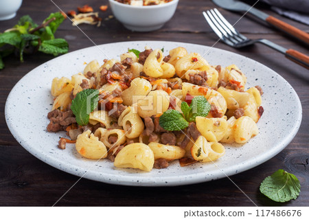 Stewed pasta with minced beef and vegetables, macaroni in Navy style on a plate. Dark wooden background. Stewed pasta with minced beef and vegetables, macaroni in Navy style on a plate. Dark wooden background. 117486676