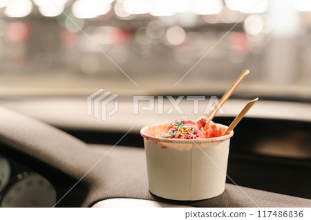 A cup of ice cream on the dashboard of a car 117486836