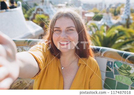 Beautiful 30s female in Gaudi garden, Spain, Barcelona. Young traveling woman taking selfie outdoors. Concept of travel, tourism and vacation in city. High quality photo Beautiful 30s female in Gaudi garden, Spain, Barcelona. Young traveling woman taking selfie outdoors. Concept of travel, tourism and vacation in city. High quality photo 117487018