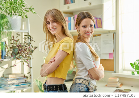 Portrait of two girls positive college students with crossed arms in home Portrait of two girls positive college students with crossed arms in home 117487103