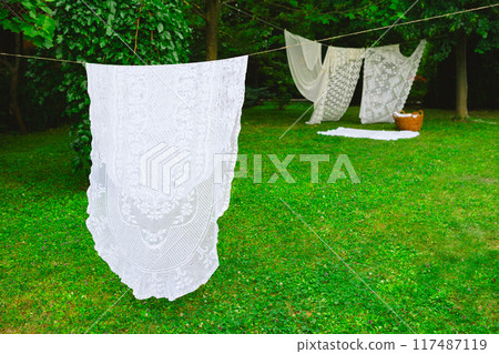 White laundry on clothesline in garden. White curtains drying in the sun. 117487119