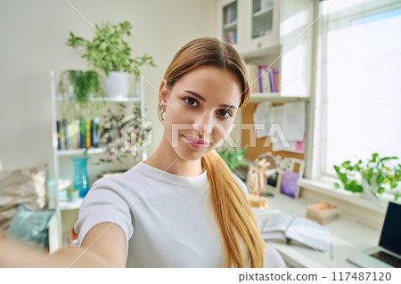 Close-up selfie portrait of teenage cheerful female looking at web camera Close-up selfie portrait of teenage cheerful female looking at web camera 117487120