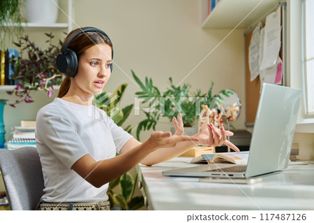Girl teenage student in headphones having video chat online on computer Girl teenage student in headphones having video chat online on computer 117487126