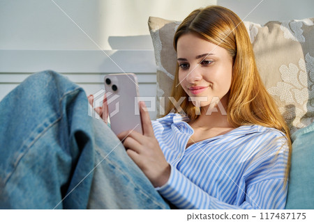 Young woman using smartphone sitting on couch at home Young woman using smartphone sitting on couch at home 117487175