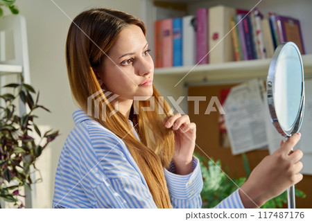 Young beautiful woman looking at face hair skin makeup teeth in mirror Young beautiful woman looking at face hair skin makeup teeth in mirror 117487176