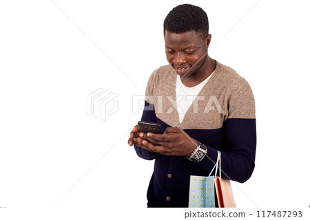 young smiling man with shopping bags is using a mobile phone 117487293