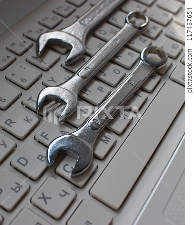 Metallic wrenches on a buttons of laptop keyboard vertical stock photo. Different types of hardware concept image Metallic wrenches on a buttons of laptop keyboard vertical stock photo. Different types of hardware concept image 117487654